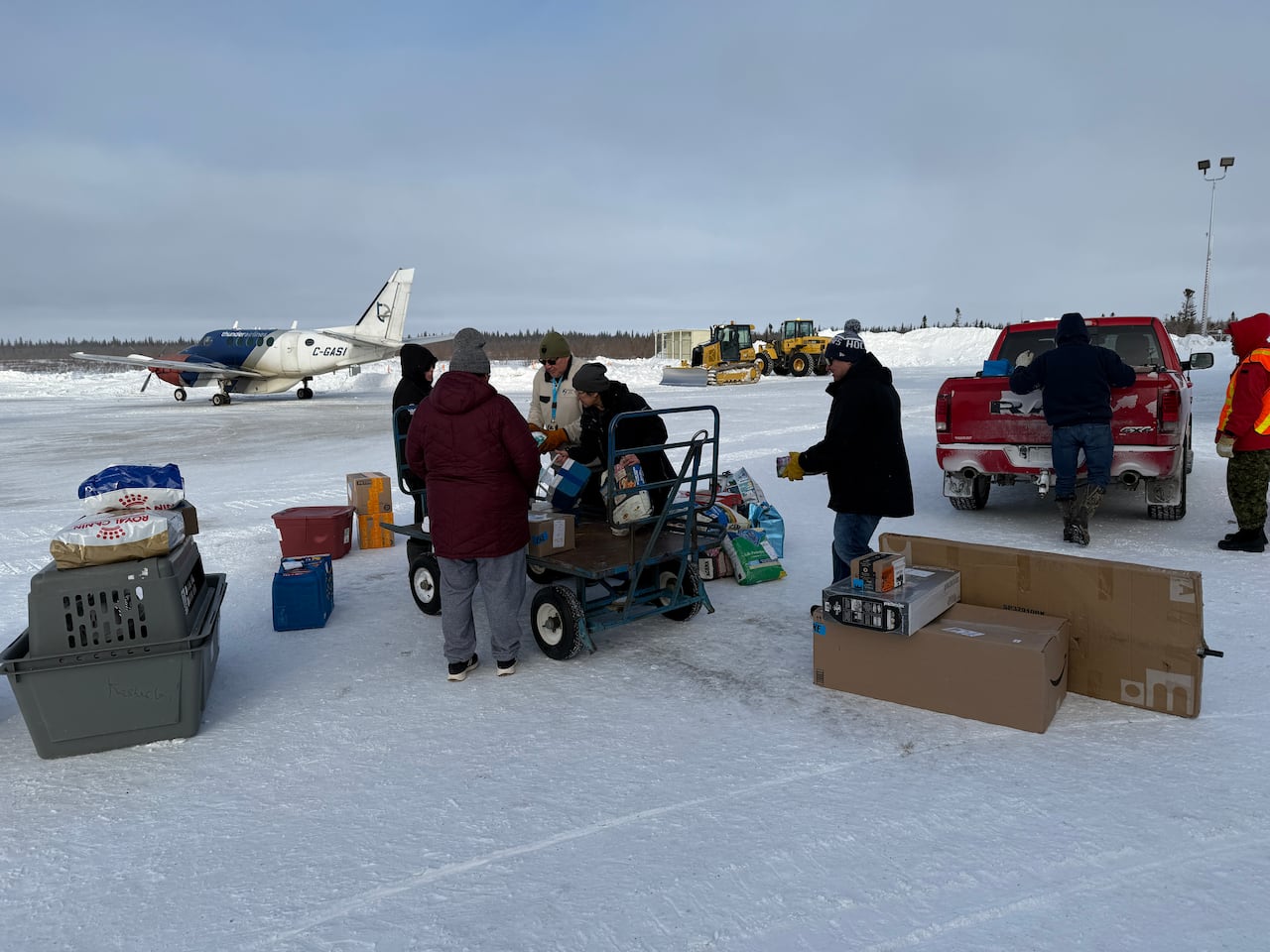 People loading a cart at an airport with a small plane in the background.