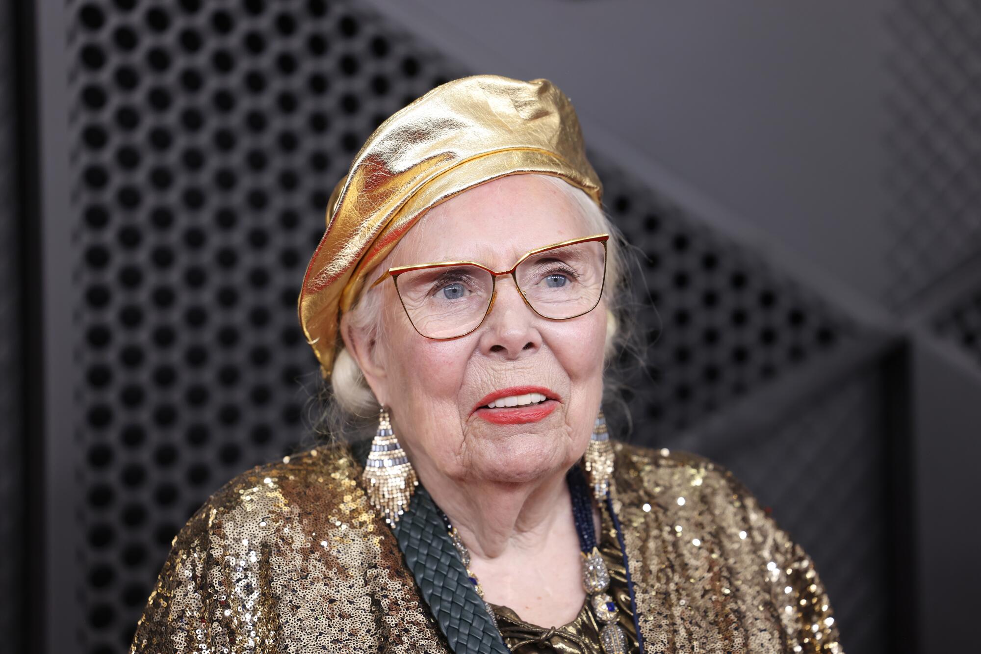 Joni Mitchell, in a gold beret, walks the red carpet. 