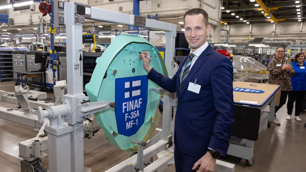A man signs a metal component and smiles.
