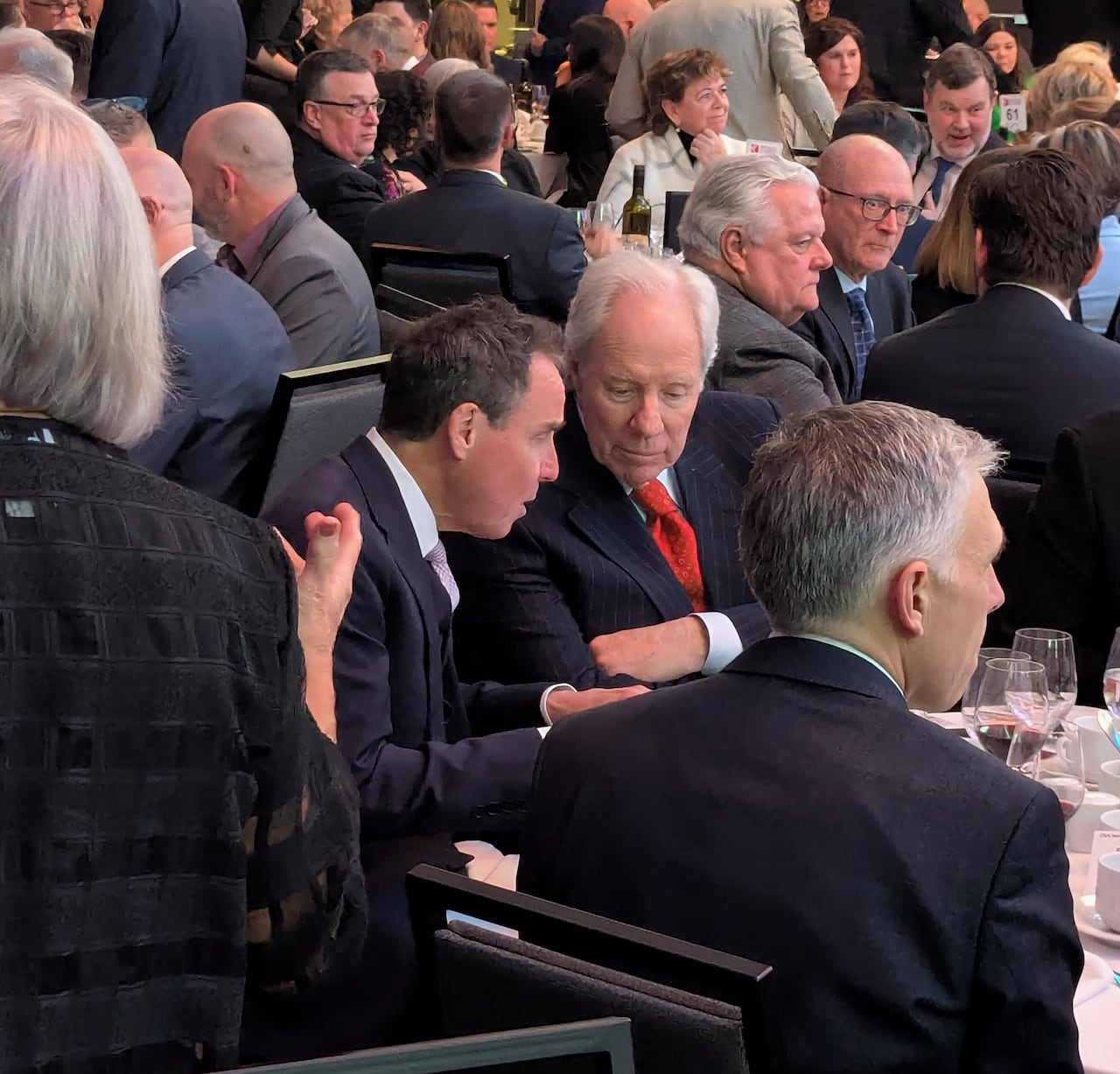 A crowd of people at a banquet with two men in the centre of the frame speaking to one another.