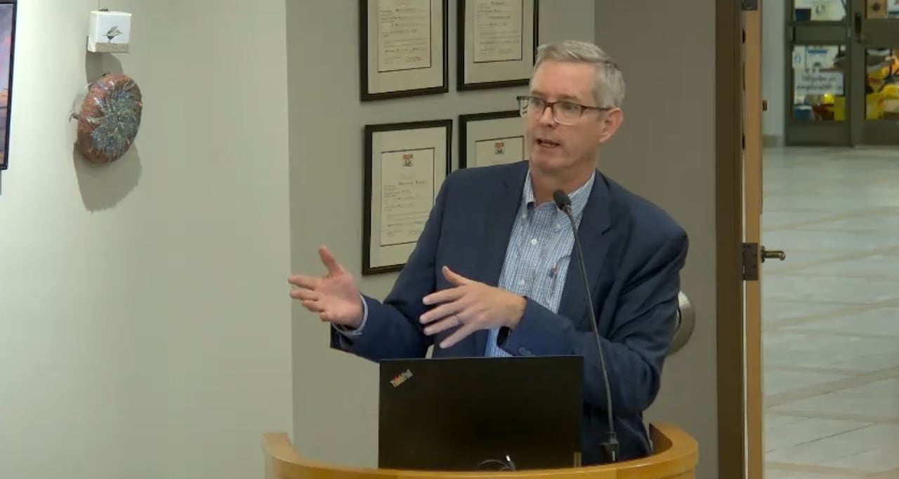 Man in blue suit speaks at wooden podium.