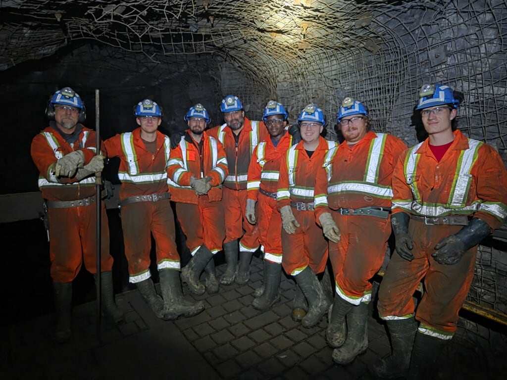 A group of mining students stand in a line in an underground drift.