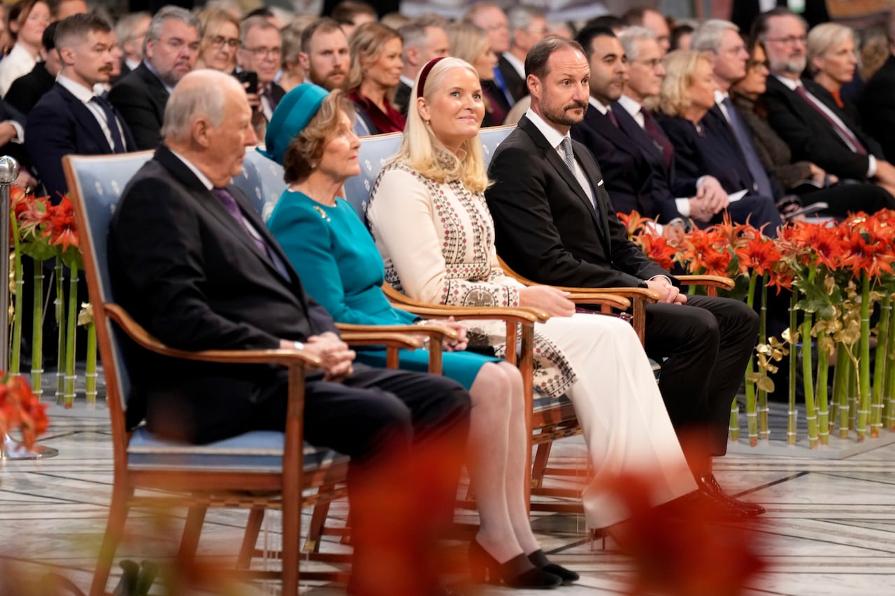 Four people in formal dress sit in chairs  in a crowd