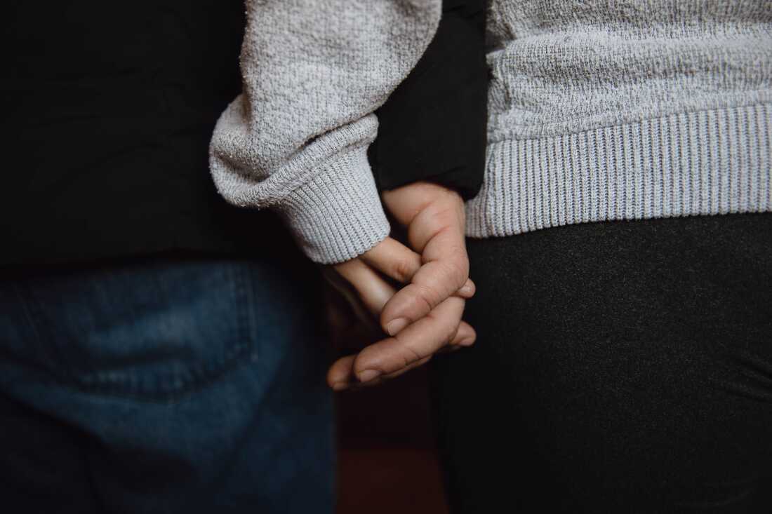 A. and her husband hold hands inside their home in Minneapolis. The Venezuelan couple, though refugees, remain fearful after federal agents detained their son.