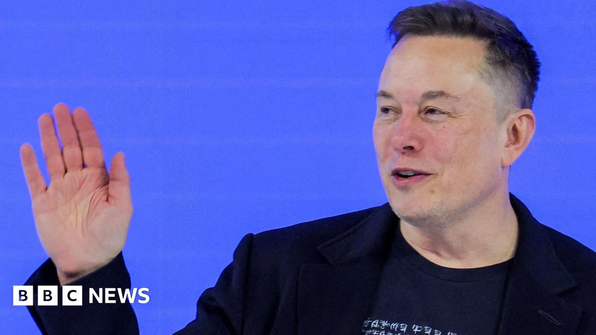 Elon Musk in a black t-shirt and black blazer waving at the audience during a conversation at this year's World Economic Forum in Davos.