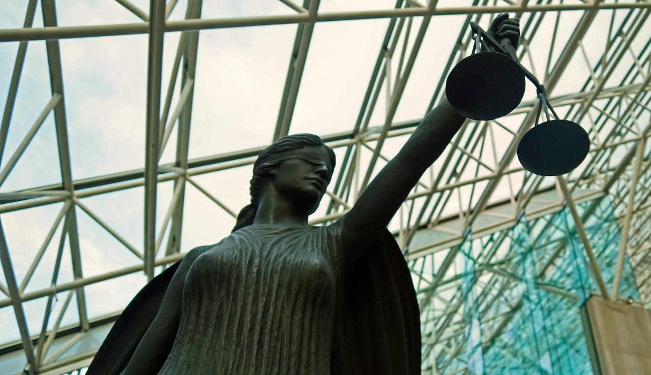 A statue of a blindfolded female figure holding a scale inside a glass-roofed building