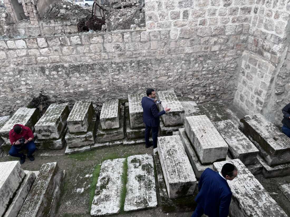 Henry Hamra examines centuries-old tombstones of rabbis buried at Aleppo’s main synagogue while his son Joseph (l) says a prayer.