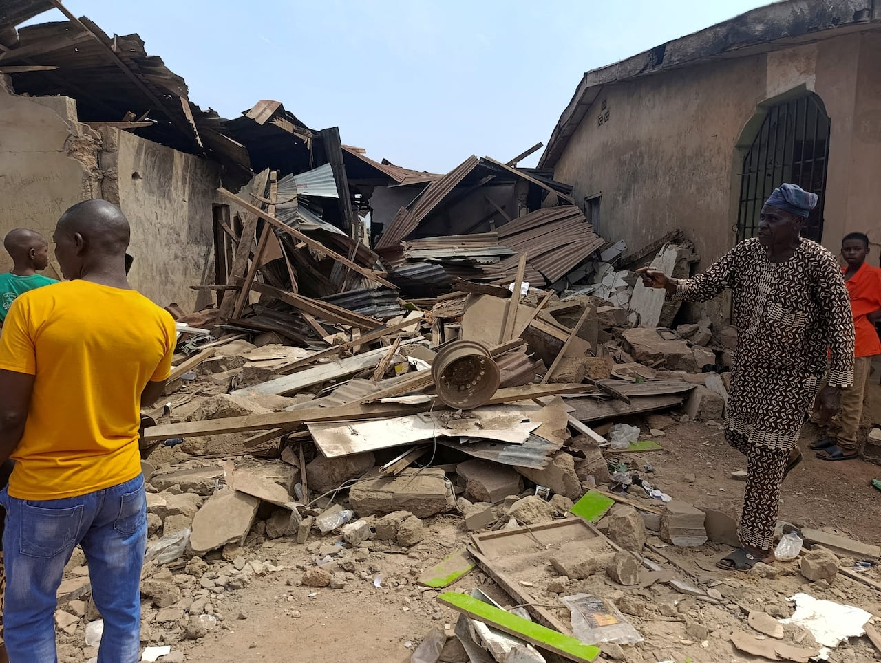 People stand near wooden and stone detritus next to a building.
