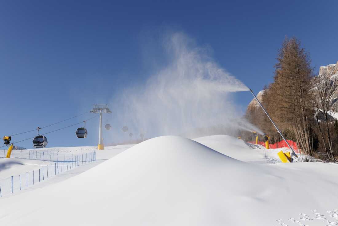 A snow cannon operates on the Socrepes slopes at the foot of the Tofane massif, producing artificial snow for the upcoming Milano Cortina 2026 Winter Olympic Games. The production of "technogenic" snow requires massive quantities of water—estimated at 2.4 million cubic meters for these Games—which is extracted from local Alpine rivers like the Boite, potentially depleting mountain aquifers and damaging sensitive aquatic ecosystems. Furthermore, the energy cost is substantial, as a vast network of high-pressure pumps and cooling systems must run continuously to maintain the pistes against rising temperatures caused by climate change
