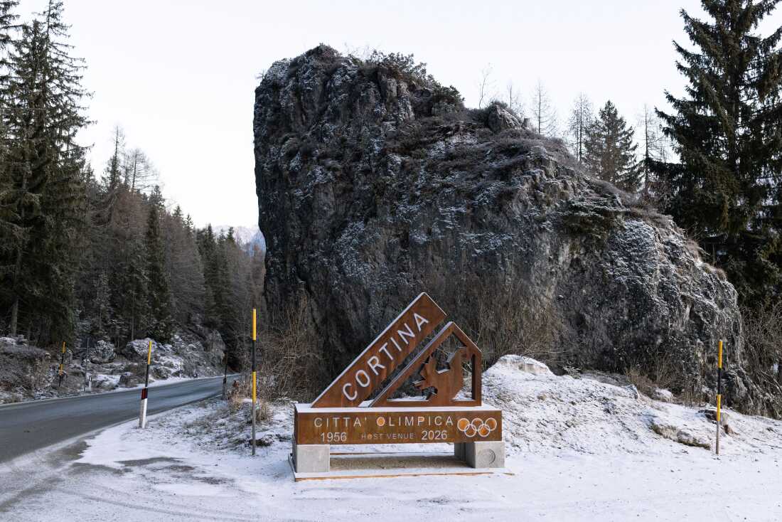 A modern corten steel monument stands along the snow-dusted arrival road, designating Cortina d’Ampezzo as a "Città Olimpica" (Olympic City). The sign commemorates both the 1956 Winter Games and its role as a host venue for the upcoming Milano Cortina 2026 Winter Olympics. While the monument symbolizes local pride, it also marks the entrance to a valley currently undergoing a controversial transformation, with nearly 100 infrastructure projects causing significant environmental concern among residents and activists