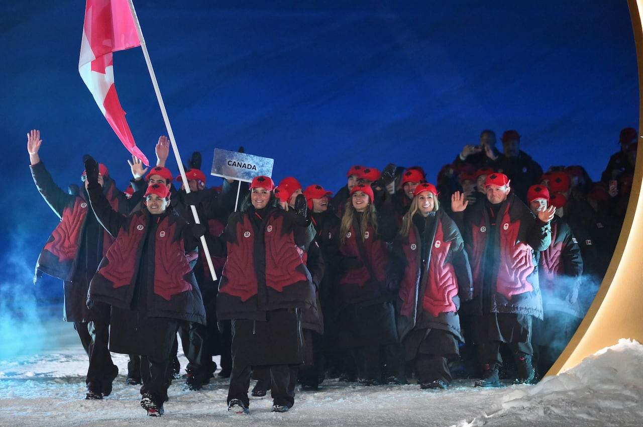 A team wearing maroon outfits with red maple leafs on puffer coats walks on stage.