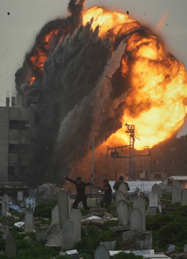 Three men take cover in a graveyard as smoke and flames rise from an Israeli military strike on a building in the Zeitoun neighborhood of Gaza City, Friday, Feb. 6, 2026. (AP Photo/Jehad Alshrafi)