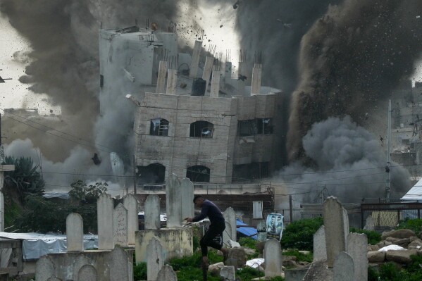 A man runs for cover in a graveyard as smoke rises from an Israeli military strike on a building in the Zeitoun neighborhood of Gaza City, Friday, Feb. 6, 2026. (AP Photo/Jehad Alshrafi)