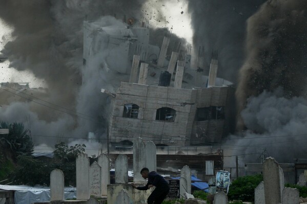 A man runs for cover through a graveyard as smoke rises from an Israeli military strike on a building in the Zeitoun neighborhood of Gaza City, Friday, Feb. 6, 2026. (AP Photo/Jehad Alshrafi)