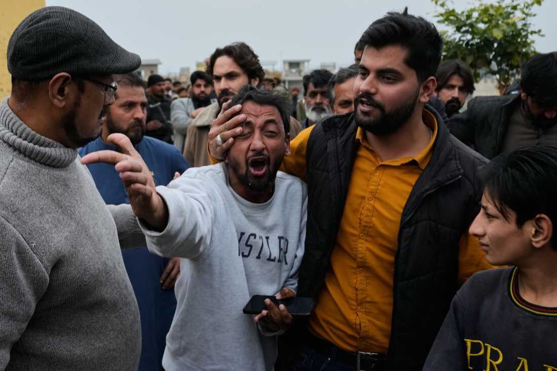People comfort a man, center, mourning over the death of his relative, close to the site of a bomb explosion at a Shiite mosque, in Islamabad, Pakistan.