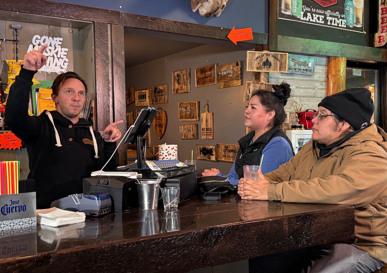 a man talks to two customers at a bar