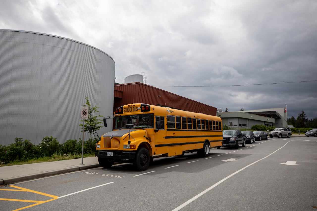 A school bus and a row of cars are parked at a high school