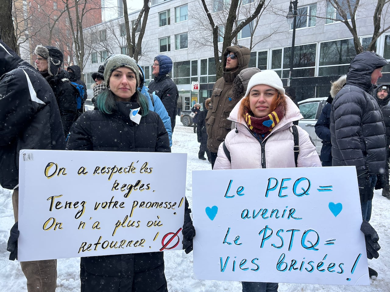 Two women stand outdoors holding protest signs. 