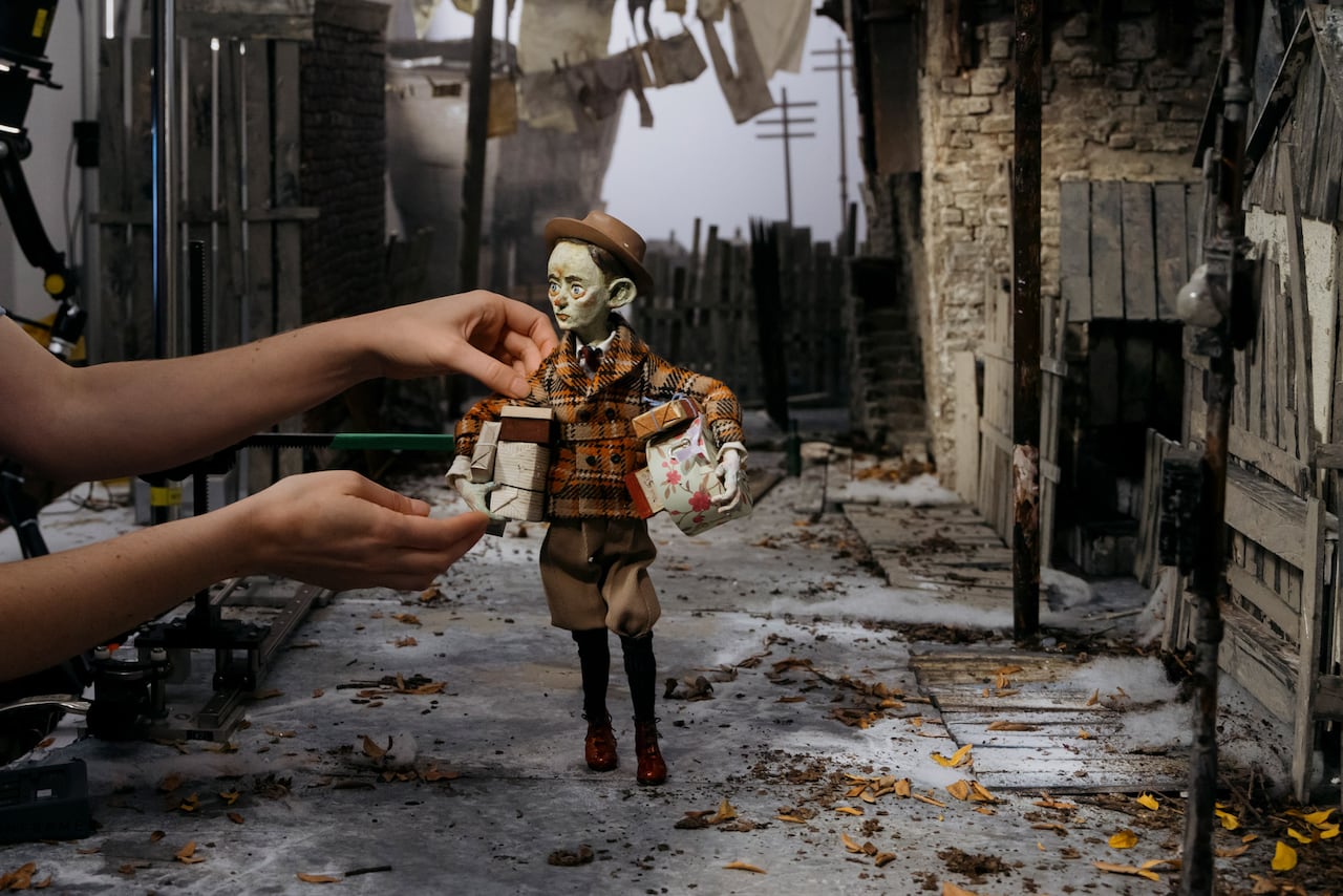 A behind the scenes photo of a pair of hands adjusting the clay character for their next take.