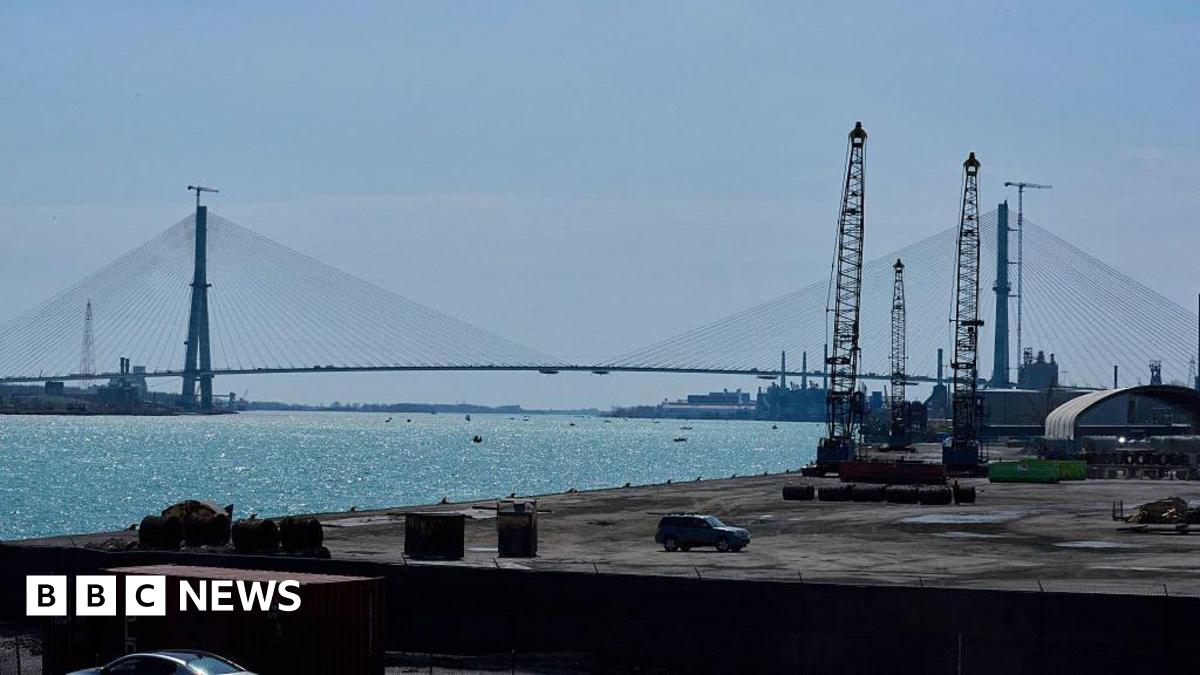 Street in Concordia, Mexico. A car and several people are in the foreground, with houses and trees on a gill in the background