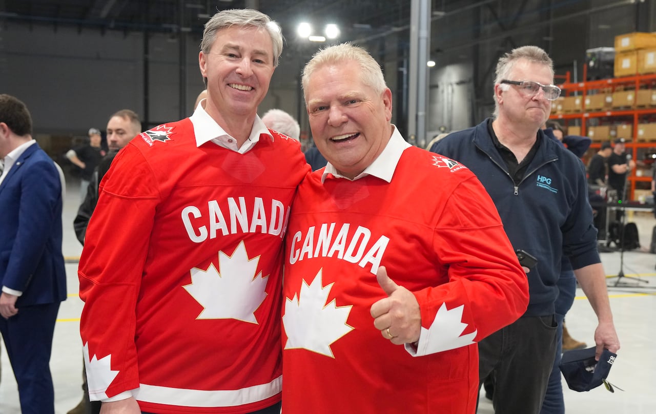 Ford and Houston stand next to one another giving the thumbs-up to the camera while wearing team Canada jerseys. 