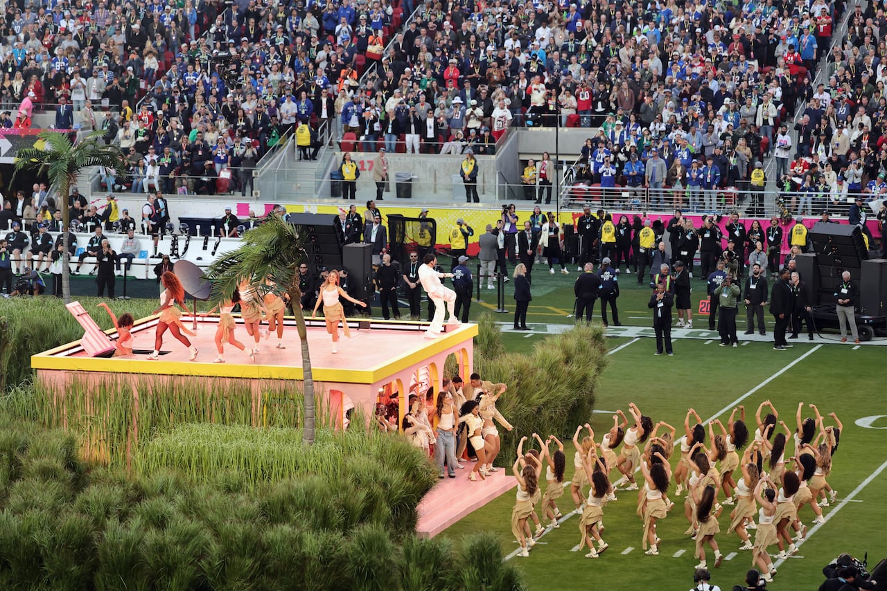 People dance and sing on and next to a pale pink white house on a football field