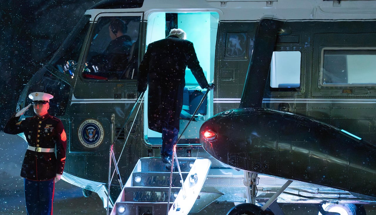 Donald Trump, seen from behind, on the steps of a helicopter on a snowy night. 