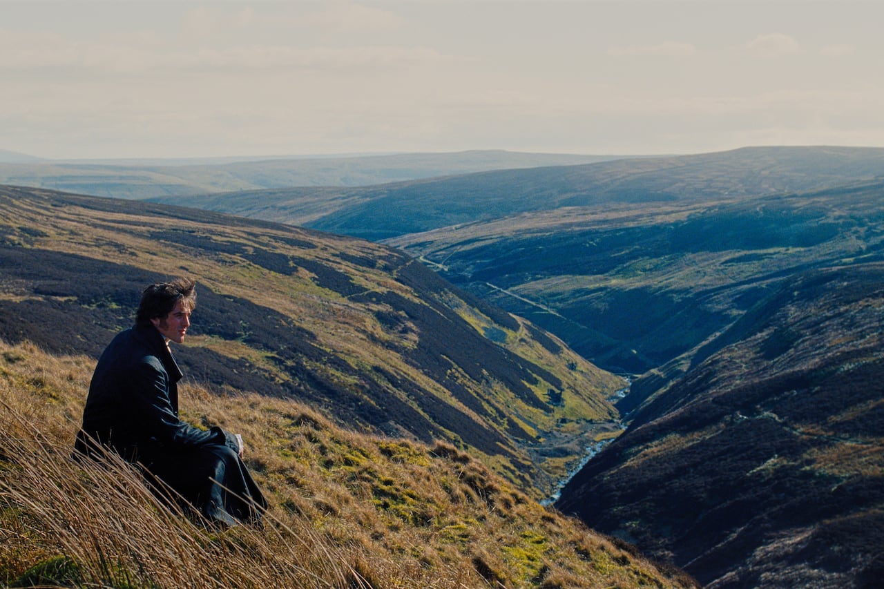 A man sits on a hill overlooking a wide grassy valley.
