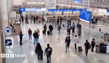 Travellers seen from above walk through the departures and check in area of an airport.