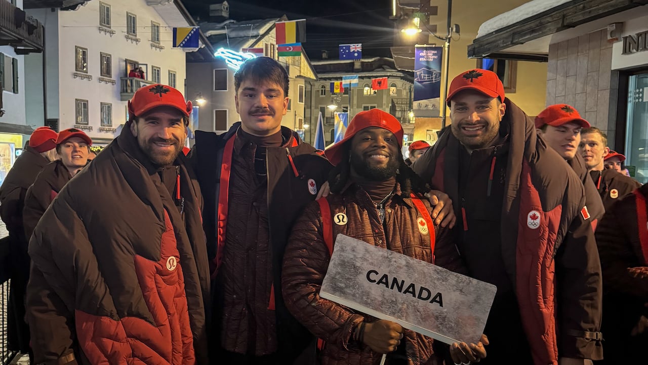 a group of people in matching winter jacket and snowpants holding Canada sign with different flags in the background