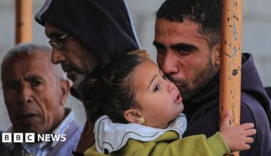 A Palestinian male mourner sheds a tear while holding on to a young child. Two other men can be seen in the background