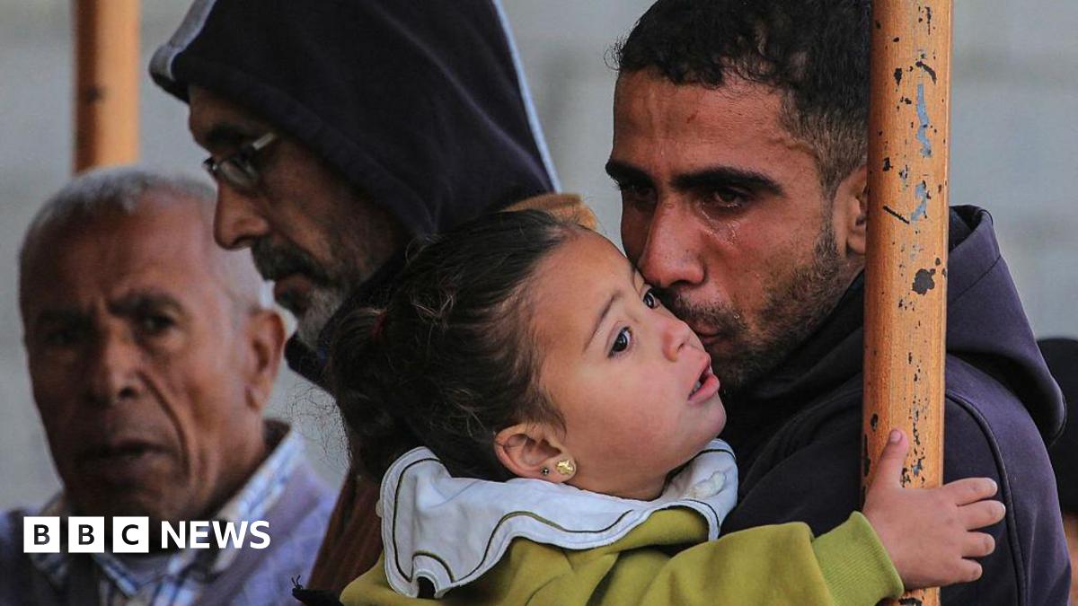 A Palestinian male mourner sheds a tear while holding on to a young child. Two other men can be seen in the background