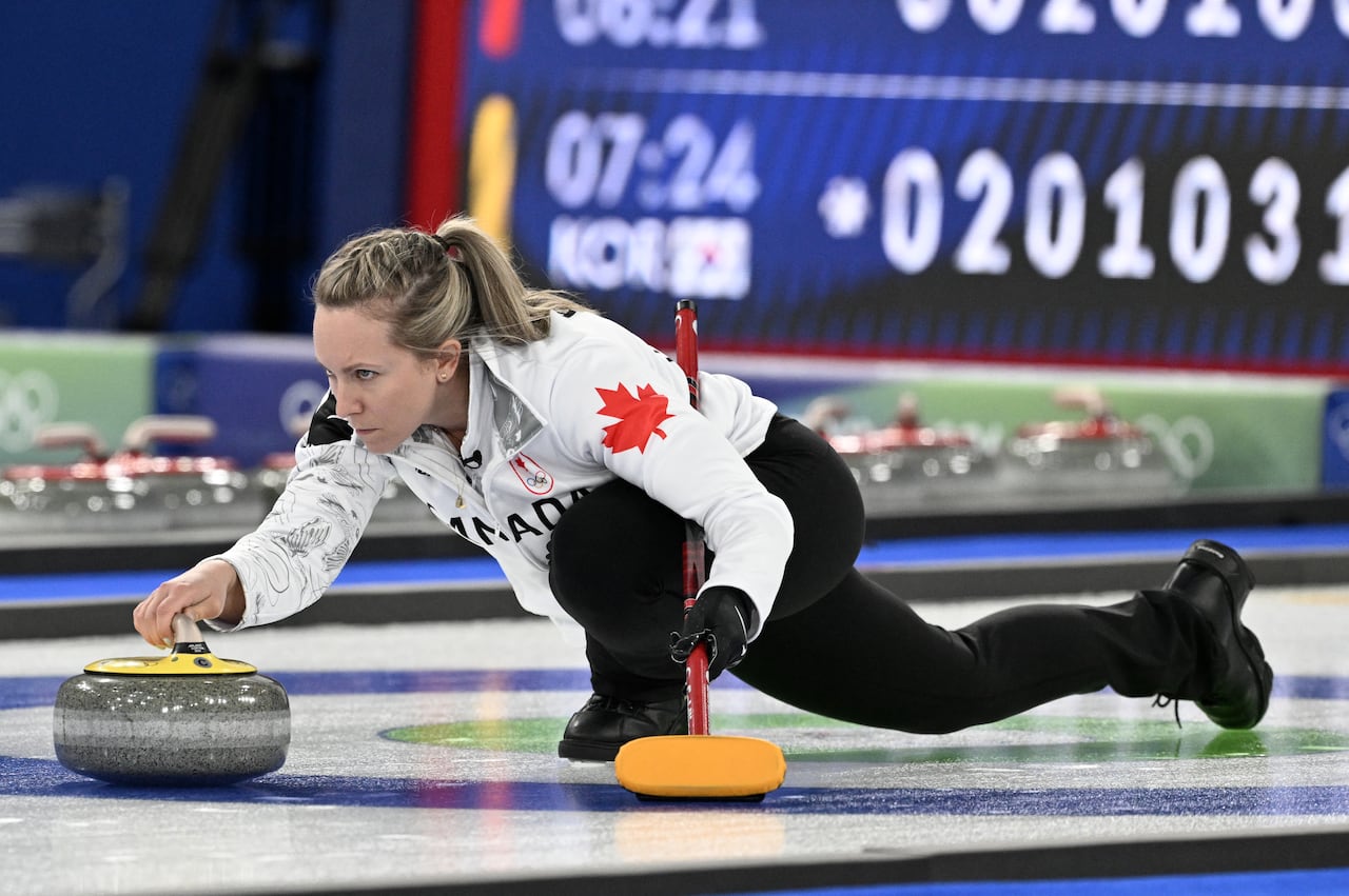 A women's curler is shown making a shot just before she releases the stone.