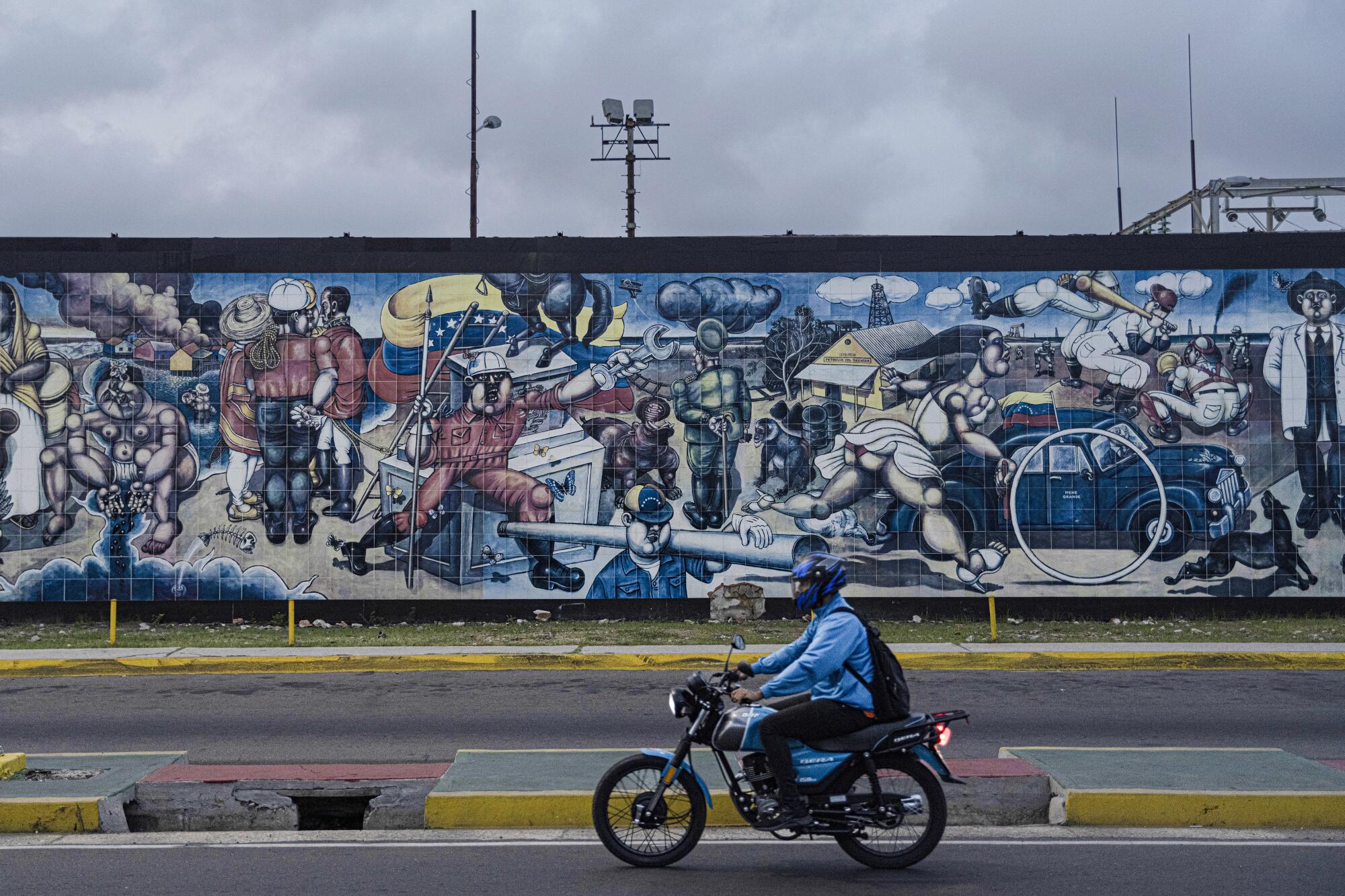 a man on a motorcycle passes a mural on Venezuelan oil topics