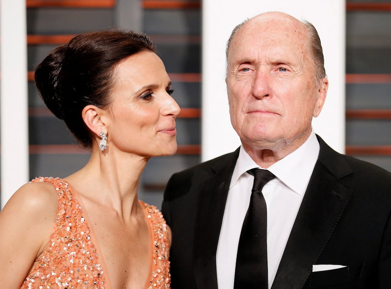 Man in a suit next to a woman dressed in a sparkling orange evening gown. She looks at him while he looks ahead