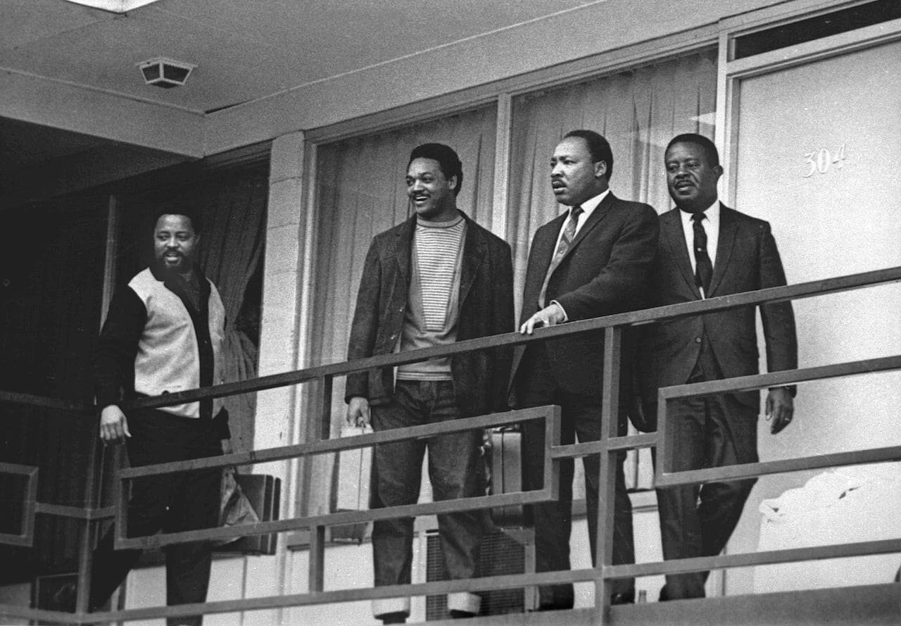 Four dark-complected men are shown on the balcony of a building in a black and white photograph that appears decades old.