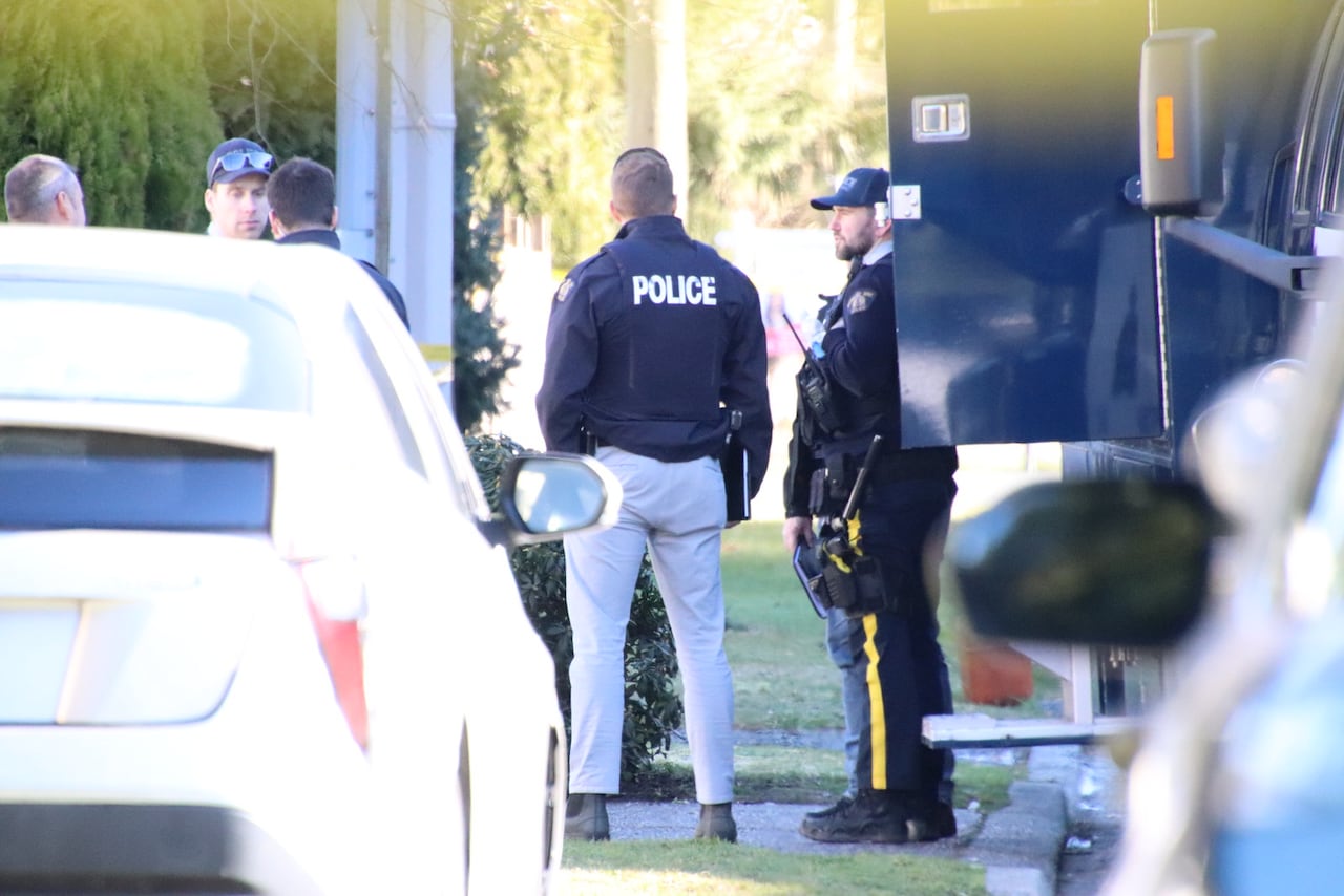 Police officers stand in a suburban lawn on a sunny day.