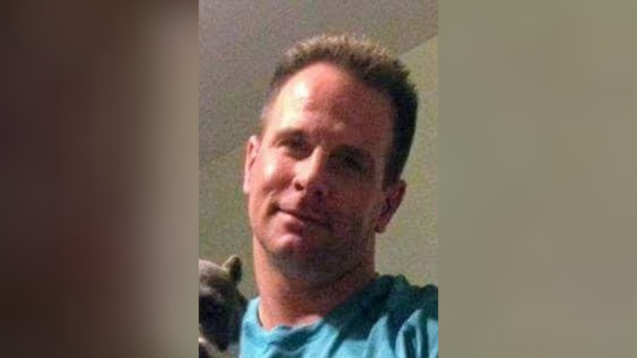 A white man wearing a blue shirt smiles.