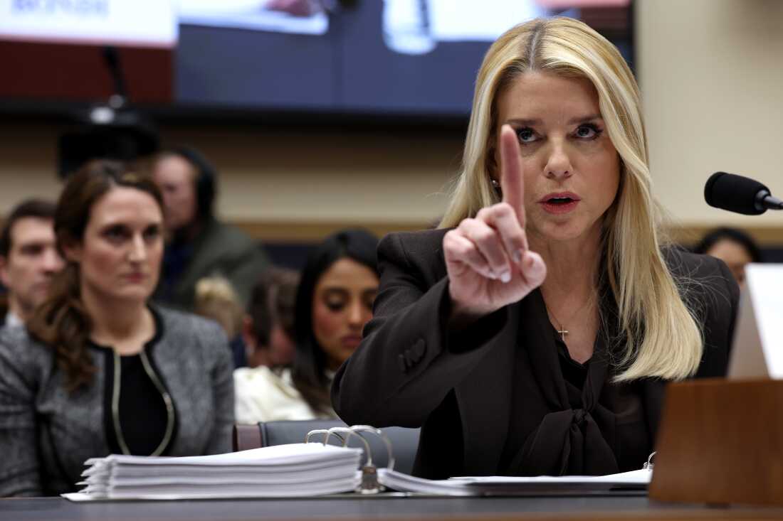 Seated behind a microphone, Attorney General Pam Bondi raises her index finger in the air while testifying before the House Judiciary Committee.