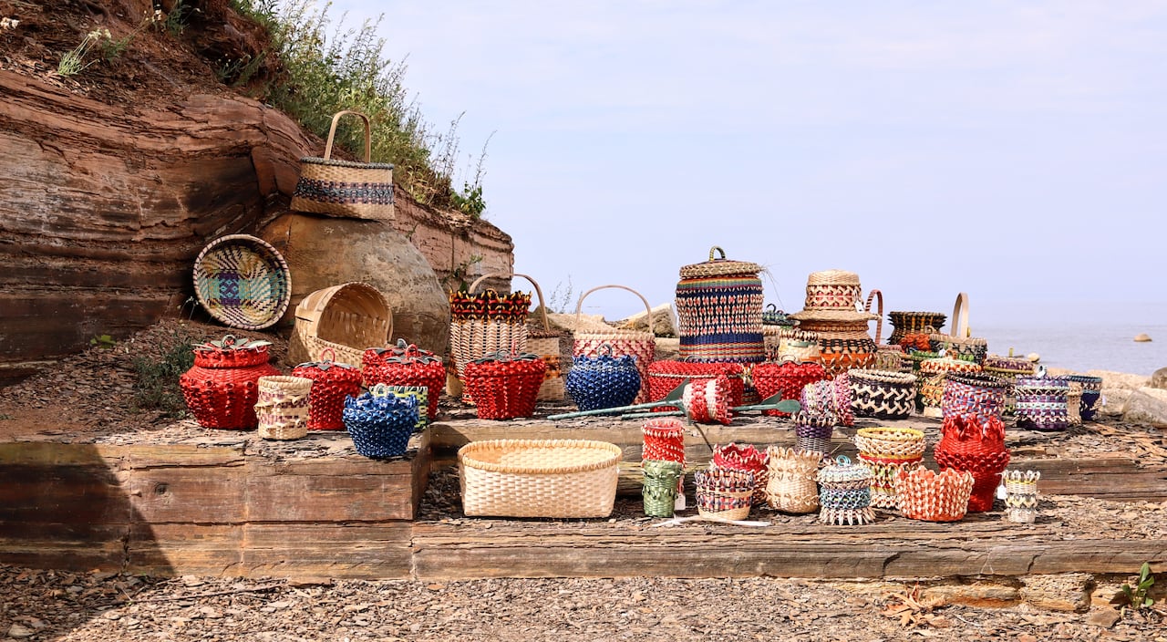 A rocky cliff by a beach, covered in around two dozen colourful intricate baskets.