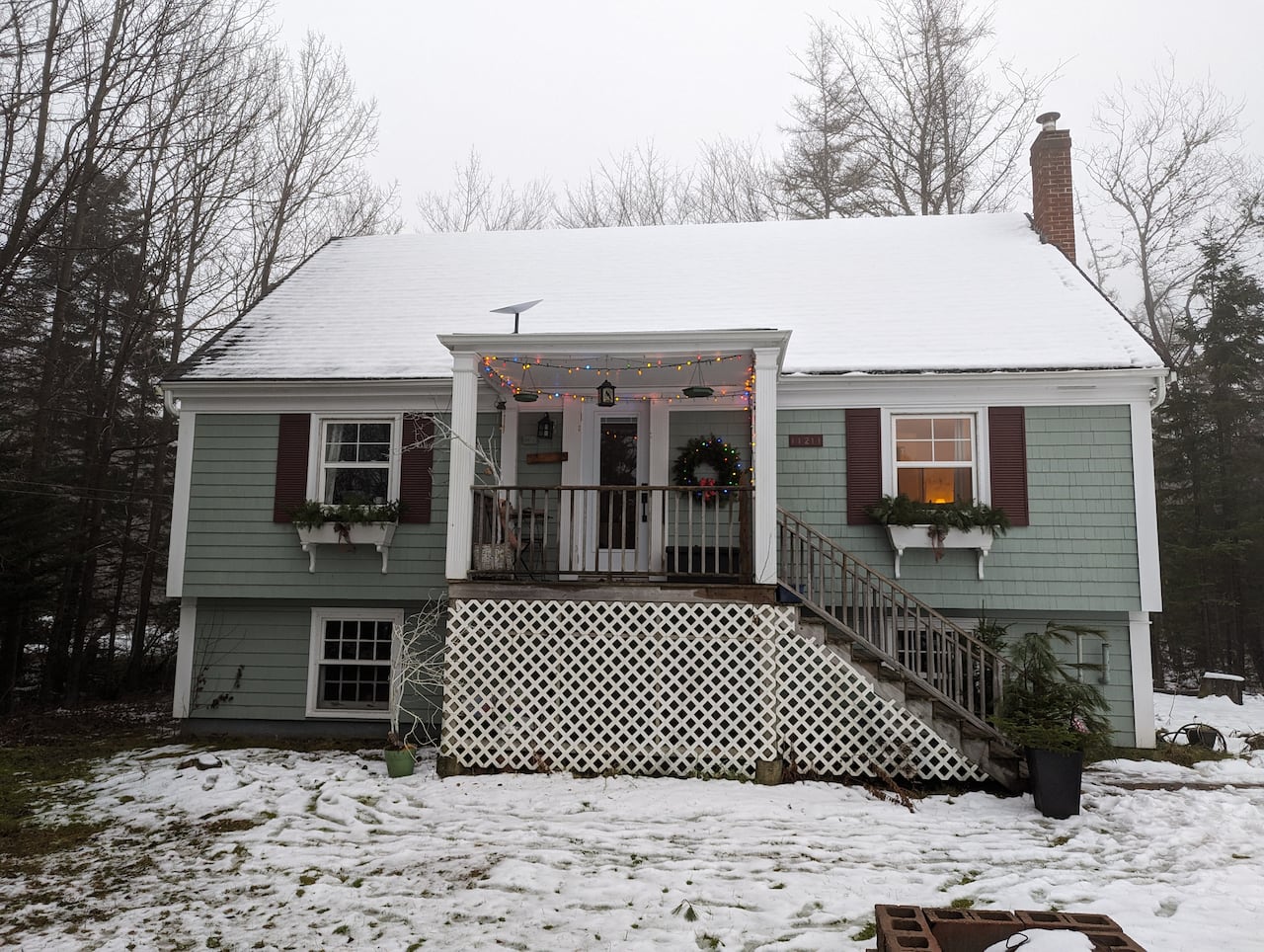 A small green house with shutters with snow on the roof and the lawn.
