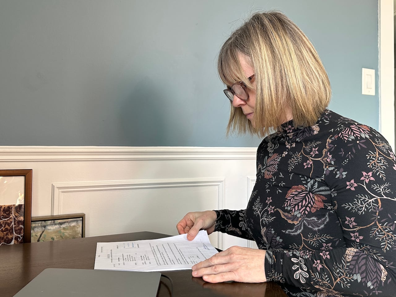 A woman in glasses looks down at a document on a table.