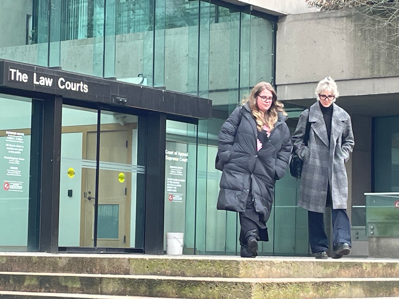 Two women in winter coats are walking away from a building with a sign saying The Law Courts.