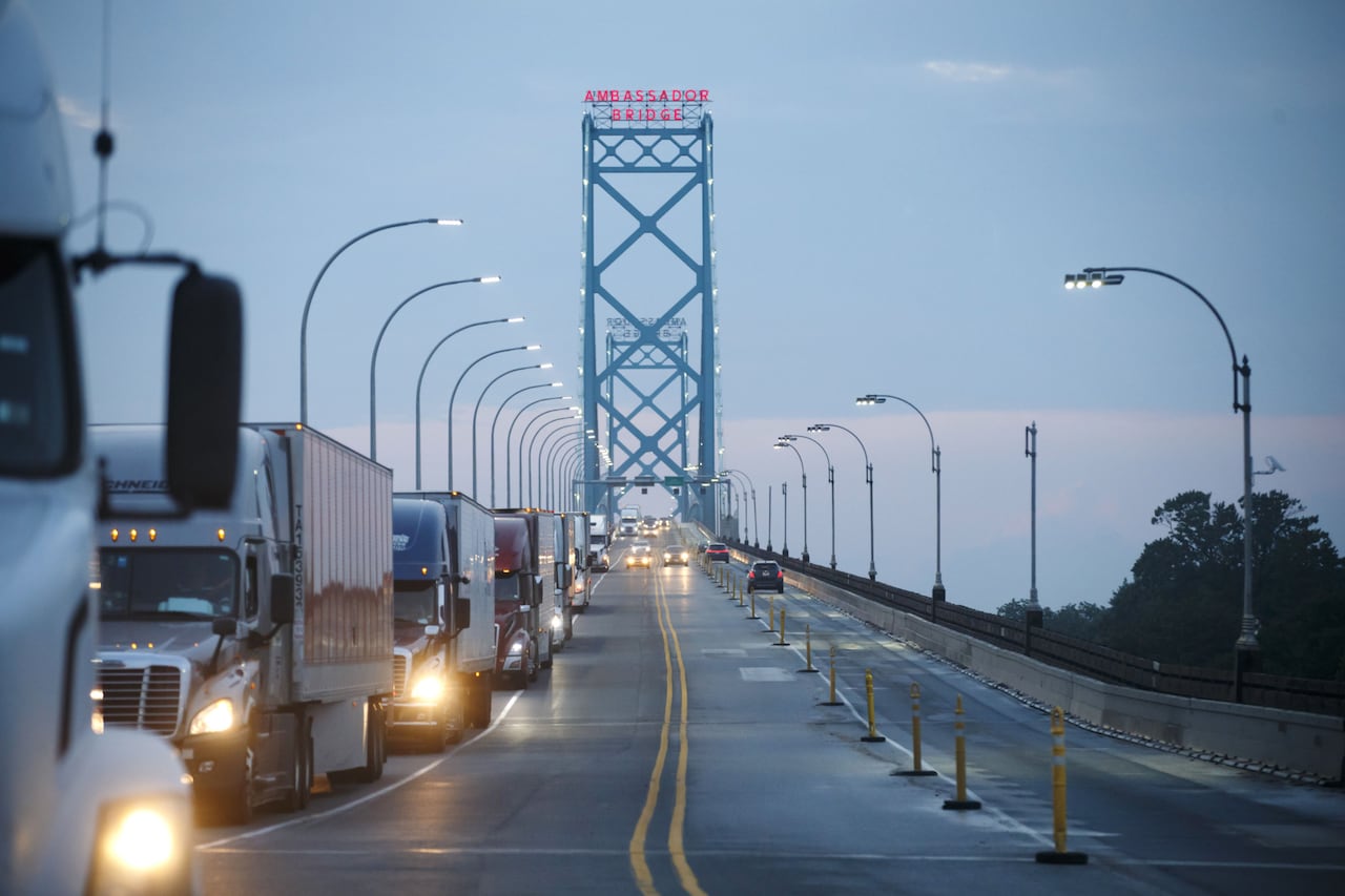 A line of cars and transport trucks forms in the oncoming lanes of a large bridge. 