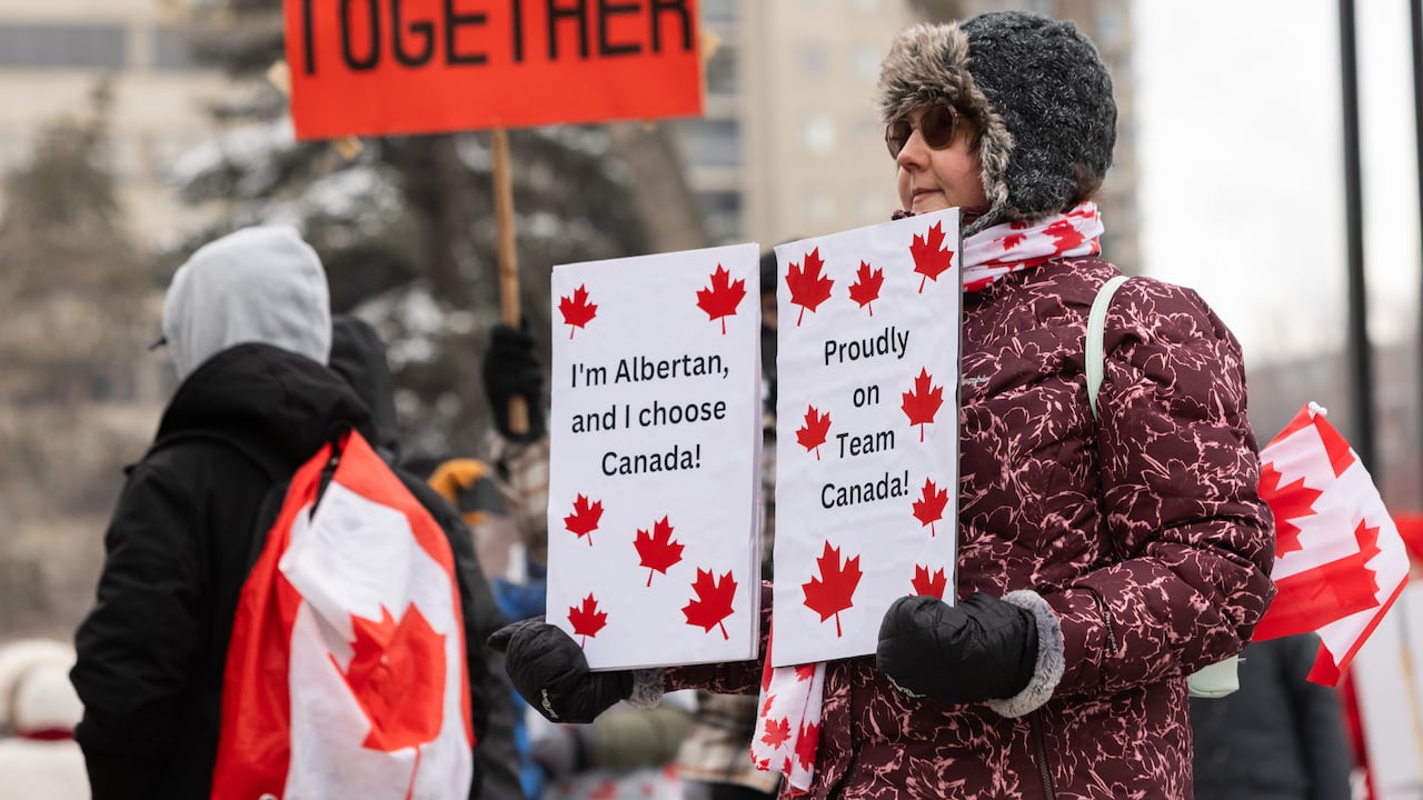 A person dressed in a jacket and warm hat holds a white sign that says: I'm Albertan, and I choose Canada!; Proudly on Team Canada!