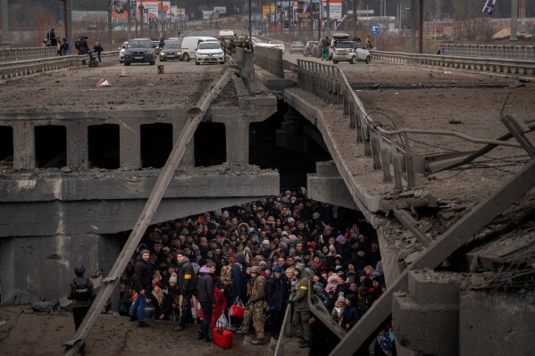 Ukrainians crowd under a destroyed bridge as they try to flee by crossing the Irpin River on the outskirts of Kyiv, Ukraine, Saturday, March 5, 2022. (AP Photo/Emilio Morenatti, File)
