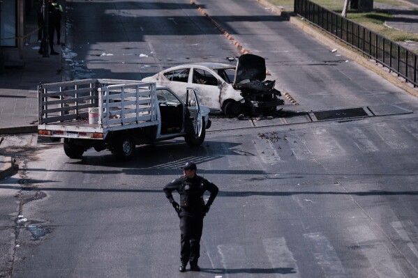 A police officer stands guard by a charred vehicle after it was set on fire, on a road in Guadalajara, Jalisco state, Mexico, Sunday, Feb. 22, 2026, after the death of the leader of the Jalisco New Generation Cartel, Nemesio Rubén Oseguera Cervantes, known as "El Mencho." (AP Photo/Alejandra Leyva)