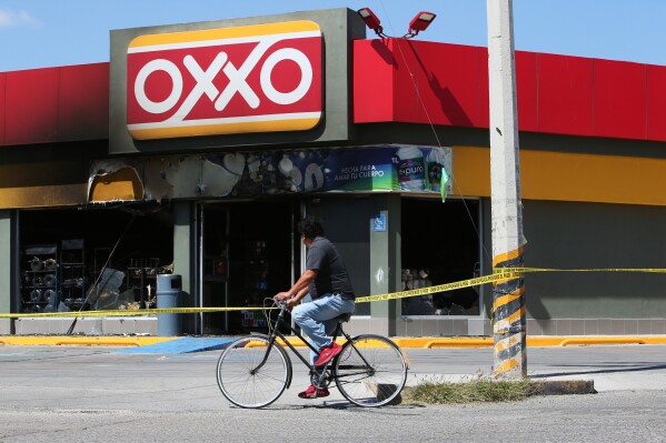 A man rides a bike next to a convenience store that was set on fire, in San Francisco del Ricon, Guanajuato state, Mexico, Sunday, Feb. 22, 2026, after the death of the leader of the Jalisco New Generation Cartel, Nemesio Ruben Oseguera Cervantes, known as "El Mencho." (AP Photo/Alfredo Valadez)