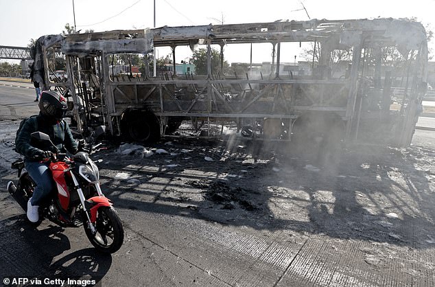 A motorcycle rides past a truck set on fire by organised crime groups in response to an operation in Jalisco to arrest a high-priority security target, at one of the main avenues in Zapopan, state of Jalisco, Mexico, on February 22, 2026. Armed civilians blocked several roads in the state of Jalisco, in western Mexico, following an operation by federal forces in the town of Tapalpa, local authorities reported. Jalisco, which will host four matches of the upcoming 2026 World Cup, is home to the powerful Jalisco New Generation Cartel (CJNG), and has been rocked by several episodes of violence in recent years. (Photo by Ulises RUIZ / AFP via Getty Images)