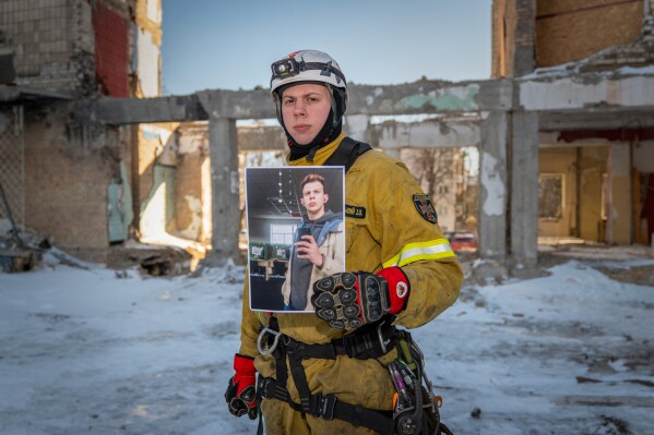 Ivan Khmelnytskyi, 25, a rescue worker, poses with a photograph of himself working in a call center before Russia's full-scale invasion, as he stands inside a residential building damaged by a Russian strike to which he responded in Kyiv, Ukraine, Saturday, Feb. 21, 2026. (AP Photo/Dan Bashakov)